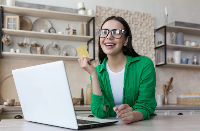 smiling woman with a credit card in hand using a laptop in her kitchen