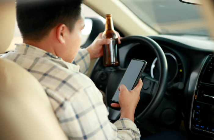 man holding a beer and using smartphone while driving