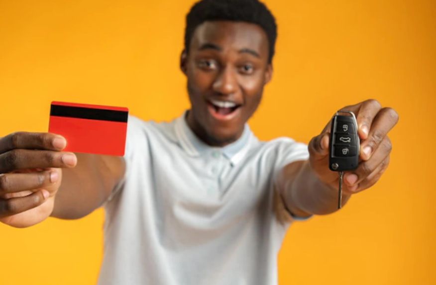 African man showing car key and credit card over yellow background