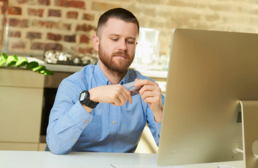 man looking at his credit card in front of his computer