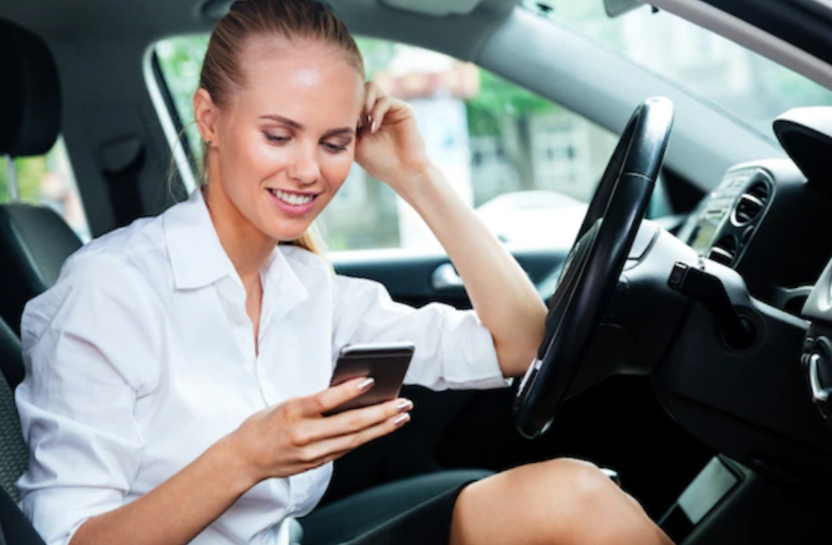 Smiling young woman dialing phone number while sitting in car
